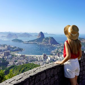 Tourism in Rio de Janeiro. Back view of traveler girl enjoying sight of famous Guanabara Bay with Sugarloaf Mountain in Rio de Janeiro, UNESCO World Heritage, Brazil.